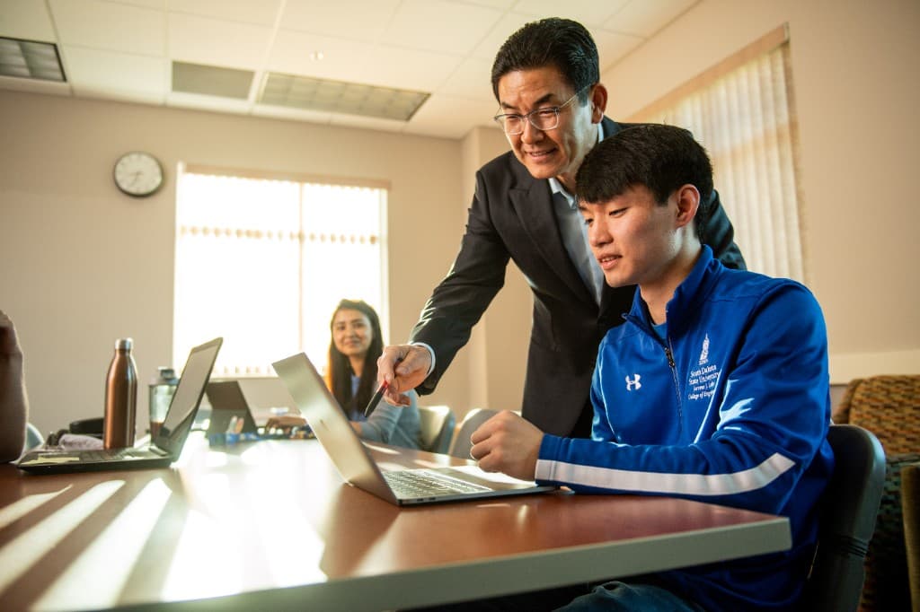 A faculty member points at a laptop while a student looks on.