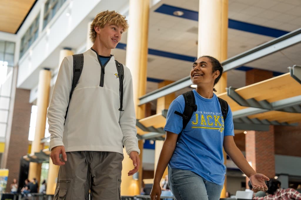 Two students with backpacks walk through a campus building.