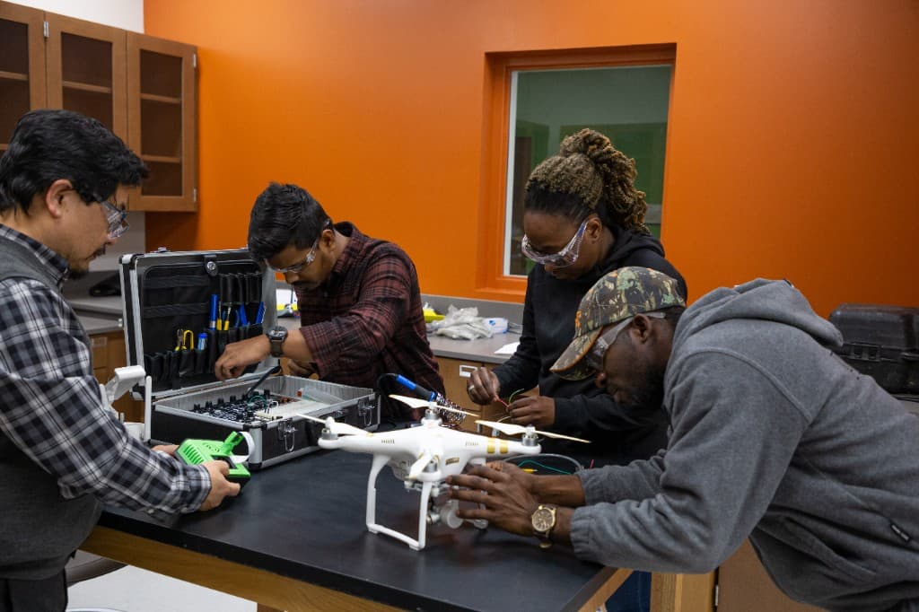 Four people work on a drone and its electronics at a lab bench.