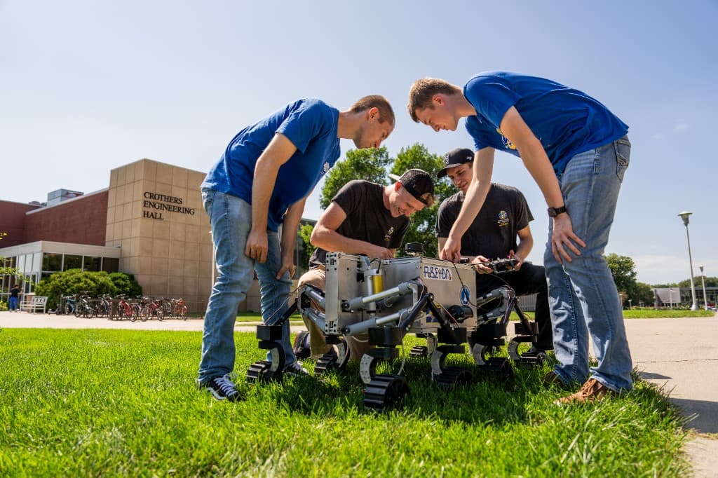 Students gather around a wheeled robot on the lawn outside Crothers Engineering Hall.