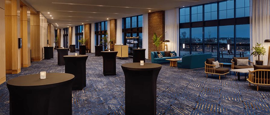 Cocktail tables in a lounge with tall windows at dusk.